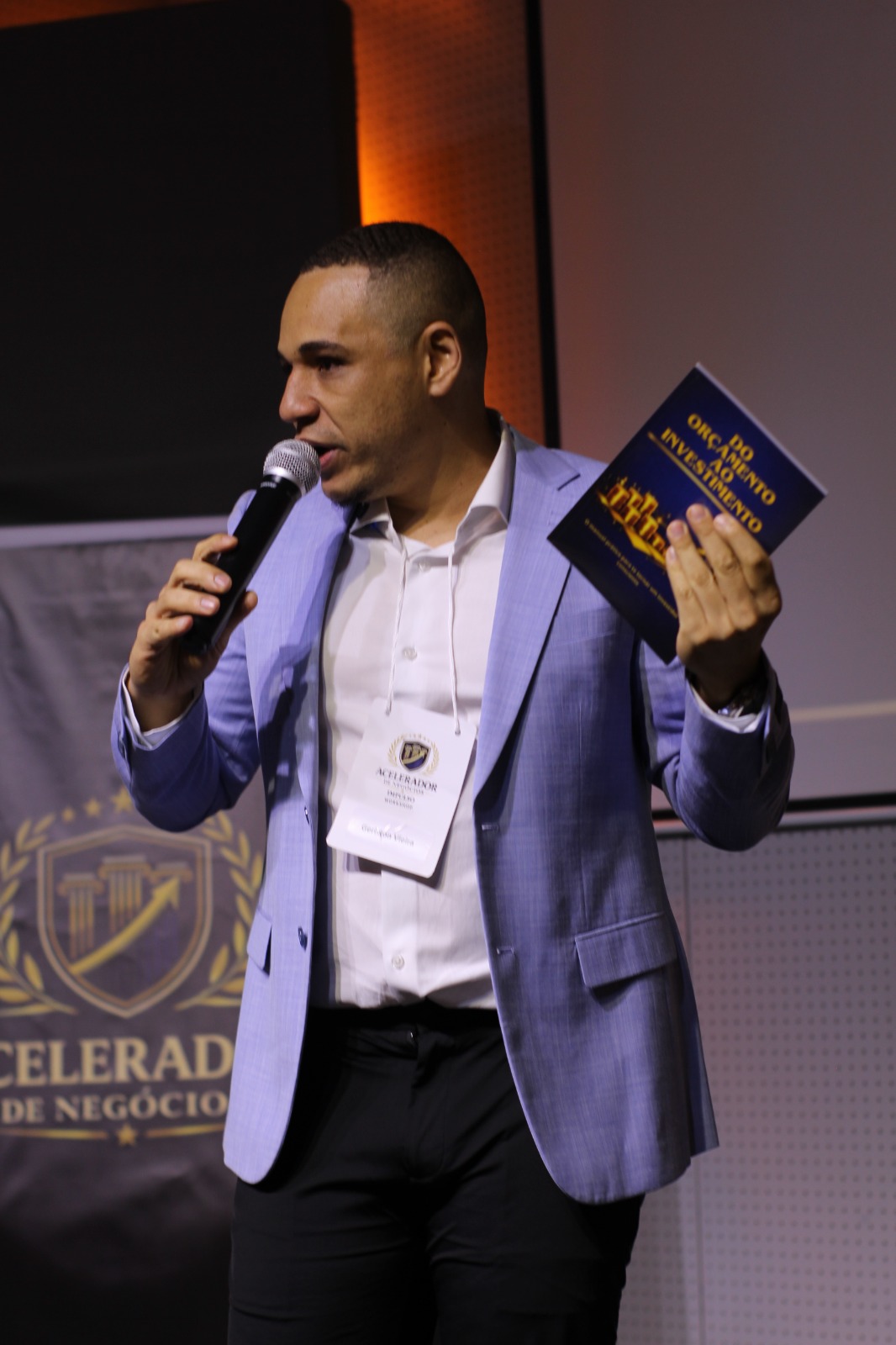 Geriston Vieira palestrando no palco segurando o livro físico